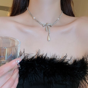 Detail of silver bow necklace with sparkling crystals and a dangling pearl pendant