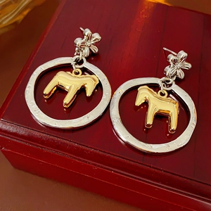 Detailed close-up of gold horse pendant inside a silver hollow circle earring on wood