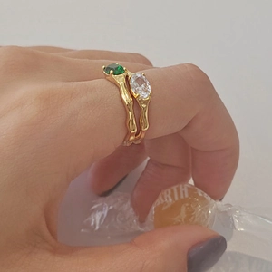 Close-up of gold wavy rings set with green and white oval cubic zirconia stones