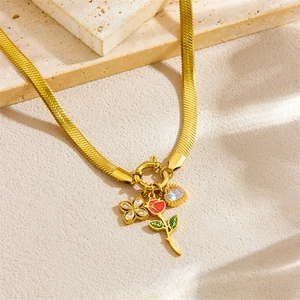 Collier chaîne serpent doré avec rose rouge, trèfle et breloques cœur sur fond de pierre