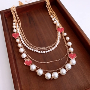 Macro detail of multi-layer gold necklace featuring white pearls and red heart pendants