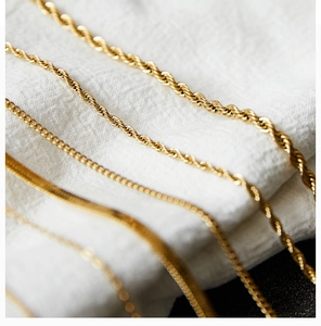 Detail shot of gold-plated titanium steel rope and curb chains on white linen fabric