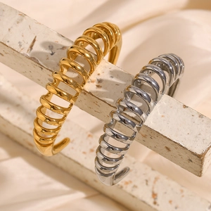 Close-up of spiral stainless steel bangles in gold and silver finish on a textured stone
