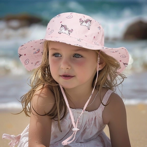 Pink toddler sun hat with unicorn pattern worn by a girl on the beach with wind strap