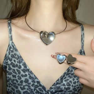 Detail showing a heart-shaped silver necklace and rings set worn by a female model