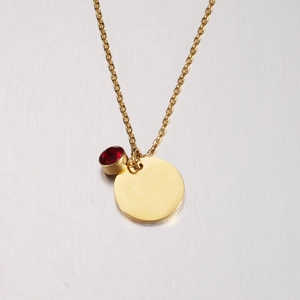 Close-up of gold mirror-finish round pendant with a red birthstone on a delicate chain