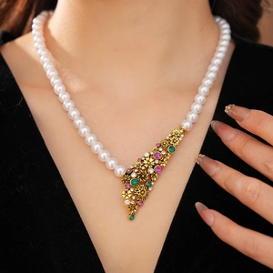 Gros plan d'un collier de perles avec un pendentif fleur dorée orné de cristaux colorés