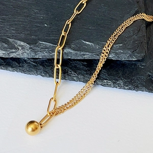Detailed view of asymmetric gold chain necklace featuring a polished solid metal ball pendant