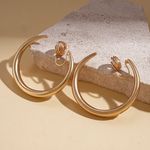 Macro view of golden C-shaped clip-on earrings with spiral back on a rustic stone pedestal