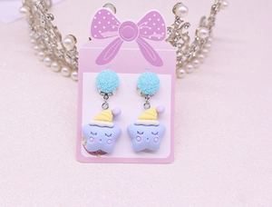 Detailed view of blue circular clip-on earrings with purple star pendants on pink card