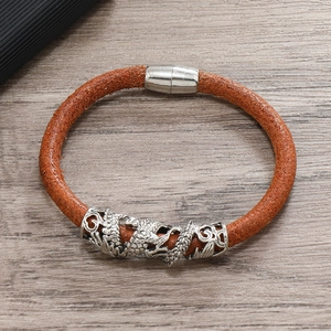 Detail of brown braided leather bracelet with engraved silver dragon charm and magnetic clasp