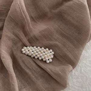 Baroque style handmade pearl hair clip with gold metal base on elegant fabric background