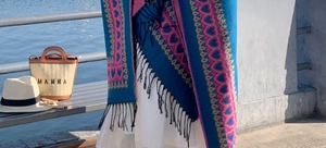 Détail d'un poncho ethnique bleu avec motifs de cœurs roses et finitions à franges