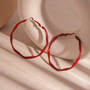 Macro detail of red twisted geometric hoop earrings with a glossy lacquered finish