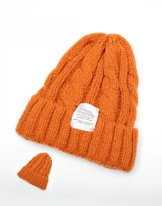 Detail of orange cable knit beanie with white woven label showing front and back view
