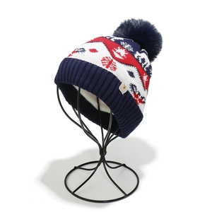 Detail of winter knit hat with reindeer and snowflake patterns and fluffy pom-pom