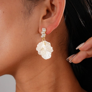 Detailed close-up of long gold earrings featuring crystals and white petal pendants