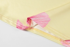 Detailed close-up of yellow satin dress fabric with pink floral print and double stitching
