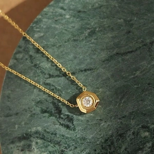 Collier géométrique doré avec pendentif diamant étincelant sur marbre vert chic
