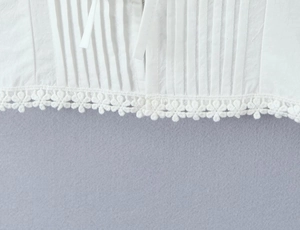 Gros plan du haut blanc avec bordure en dentelle florale et détails de tissu plissé
