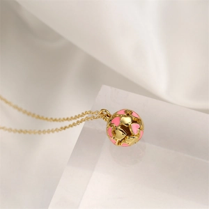 Detailed macro view of a gold necklace with a pink enamel heart-shaped spherical pendant