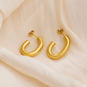 Close-up of gold-plated U-shaped oval earrings on a beige silk fabric background