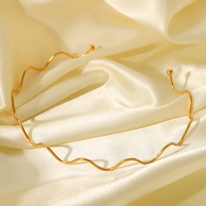 Detail of 18K gold wave pattern necklace on soft yellow silk showing glossy metal texture