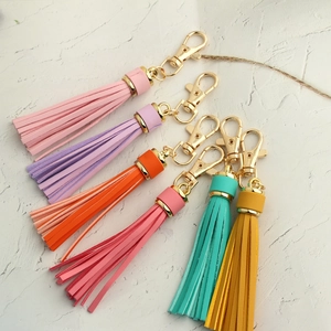 Flat lay of six colorful leather tassels with golden lobster clasps on white surface