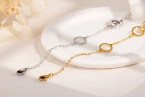 Detail of elegant gold and silver chain bracelets with polished circle pendants on ceramic