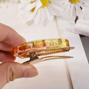 Detalle de pinza de resina con degradado amarillo-naranja y base de metal dorado