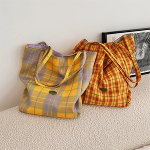 Detail of reversible plaid canvas tote bags in yellow and purple on a soft sofa