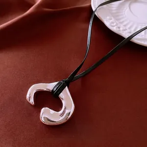 Irregular silver C-shape metal pendant on black leather cord over red silk background