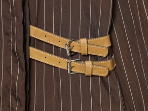 Detail shot of brown striped shirt featuring tan leather buckle straps and silver hardware