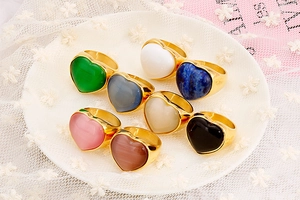 Set of eight gold heart rings with colorful resin stones arranged on a white textured plate