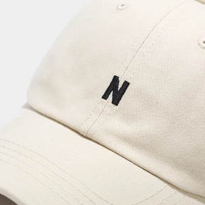 Minimalist beige baseball cap featuring a black embroidered N logo in a detailed close-up