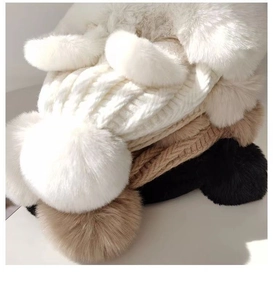 Detail showing multiple colors of cable knit hats with large fluffy faux fur pom-poms