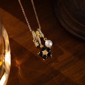 Macro detail of gold necklace with black stone flower, pearl pendant and clear zircon