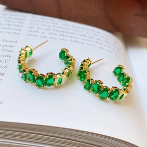 Dettaglio di orecchini a cerchio dorati con cristalli verde smeraldo su un libro