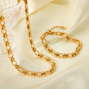 Detail of 18K gold-plated stainless steel necklace and bracelet set on silk background