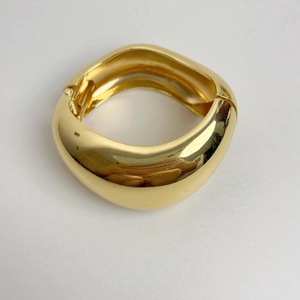Makroaufnahme einer breiten goldenen Gelenkspange aus Metall mit Hochglanzoberfläche