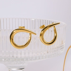 Polished 18k gold-plated C-shaped stainless steel earrings on a glass rim