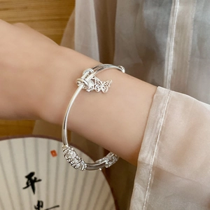 Detail of silver bamboo bracelet with floral carving and a hollow butterfly charm pendant