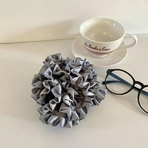 Close-up of a grey pleated silk scrunchie on a white table with a teacup and glasses