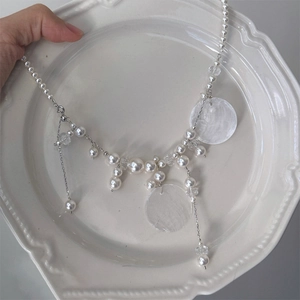 Detail of shell pearl tassel necklace with silver chain on a white ceramic plate