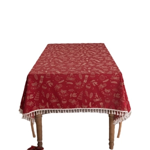 Red Christmas tablecloth with gold bells and white tassels on a clean wood table