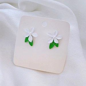 Detail of white flower earrings with green leaves and pearls on silk background