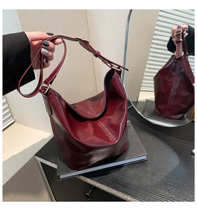 Detail of burgundy glossy PU leather bucket bag with golden hardware on a dark desk