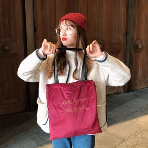 Detail of burgundy velvet tote bag with gold love rewards the brave embroidery