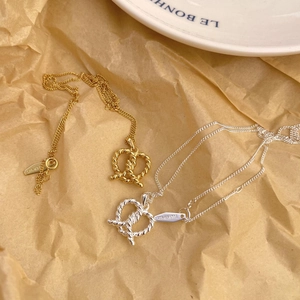 Detailed view of silver and gold pretzel heart necklaces on textured craft paper background
