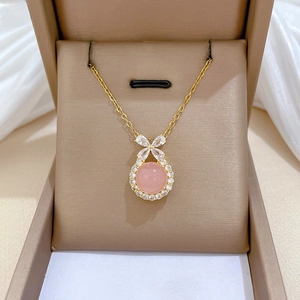 Macro shot of gold necklace with pink gemstone and crystal bow pendant in a gift box